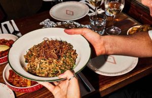 Bowl of mushroom risotto being passed over the table with two people holding